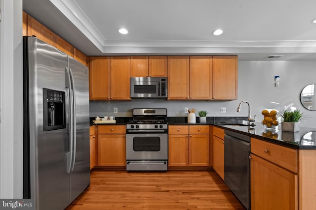 kitchen featuring sink, ornamental molding, light wood-type flooring, dark stone counters, and appliances with stainless steel finishes