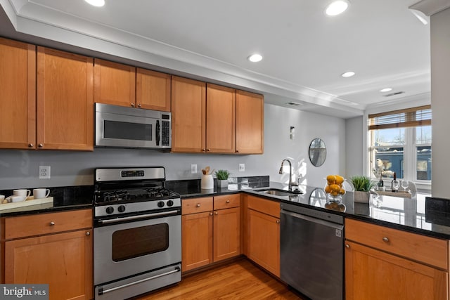 kitchen with kitchen peninsula, light wood-type flooring, appliances with stainless steel finishes, dark stone countertops, and sink