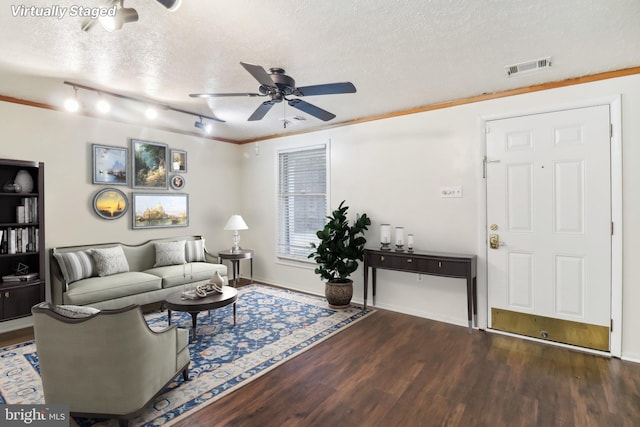 living room featuring ceiling fan, dark hardwood / wood-style flooring, ornamental molding, and a textured ceiling