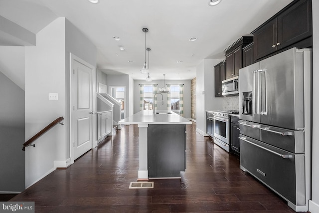 kitchen featuring sink, a kitchen island with sink, hanging light fixtures, premium appliances, and dark hardwood / wood-style flooring