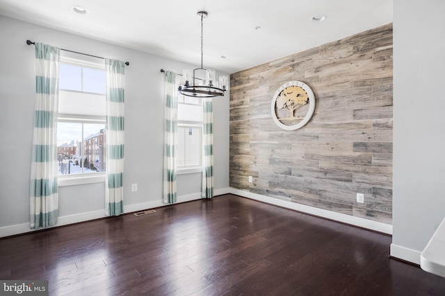 unfurnished dining area with a notable chandelier, dark wood-type flooring, a healthy amount of sunlight, and wood walls