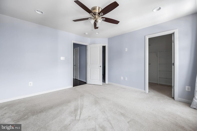 unfurnished bedroom with a walk in closet, light colored carpet, a closet, and ceiling fan