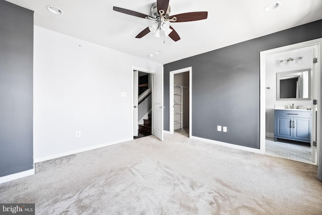 unfurnished bedroom featuring ensuite bathroom, sink, a spacious closet, ceiling fan, and light carpet