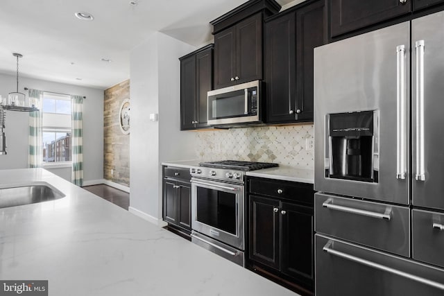 kitchen with decorative light fixtures, a chandelier, appliances with stainless steel finishes, light stone countertops, and backsplash