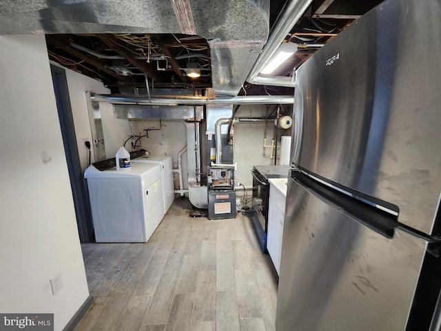 basement featuring washing machine and dryer, stainless steel fridge, heating unit, and light wood-type flooring