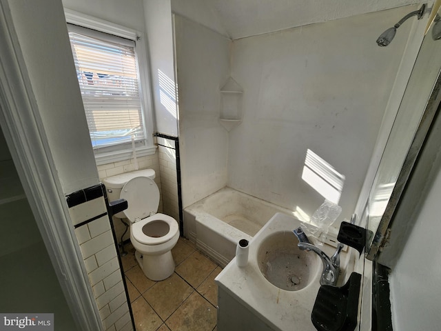 bathroom with toilet, tile patterned floors, tile walls, and sink