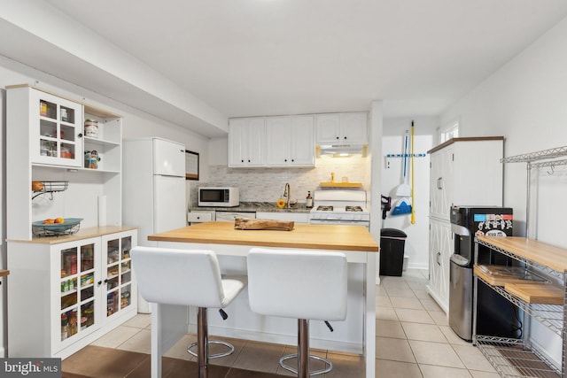 kitchen featuring white appliances, a kitchen breakfast bar, light tile patterned floors, and white cabinetry