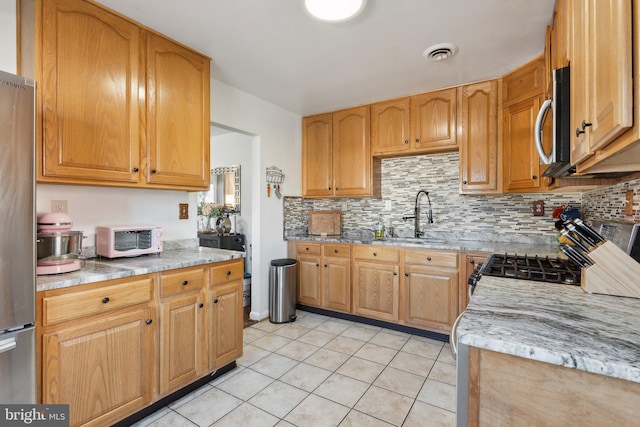 kitchen with backsplash, appliances with stainless steel finishes, light stone counters, sink, and light tile patterned flooring