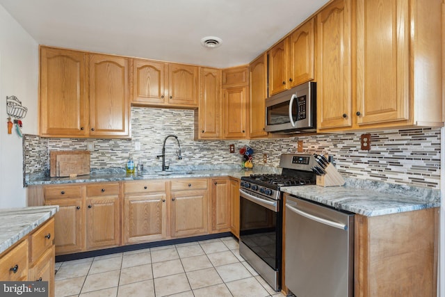 kitchen with appliances with stainless steel finishes, light stone countertops, light tile patterned floors, sink, and backsplash