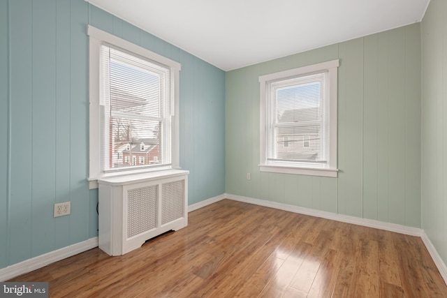 empty room with radiator heating unit, light hardwood / wood-style floors, and a healthy amount of sunlight