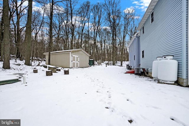 yard layered in snow with central AC and a shed