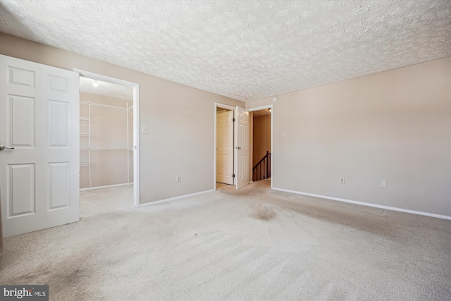 unfurnished bedroom featuring a textured ceiling, light colored carpet, a spacious closet, and a closet