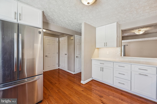 kitchen featuring wood-type flooring, stainless steel fridge, a textured ceiling, white cabinetry, and tasteful backsplash