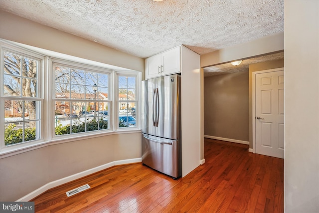 kitchen featuring white cabinets, a textured ceiling, stainless steel refrigerator, and dark wood-type flooring