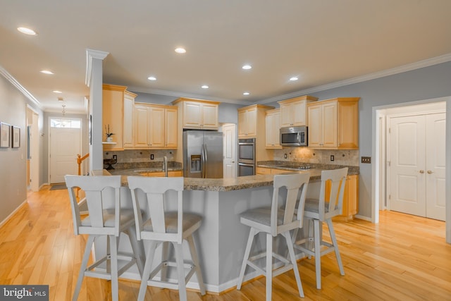 kitchen featuring light brown cabinets, stainless steel appliances, a kitchen breakfast bar, and a center island with sink