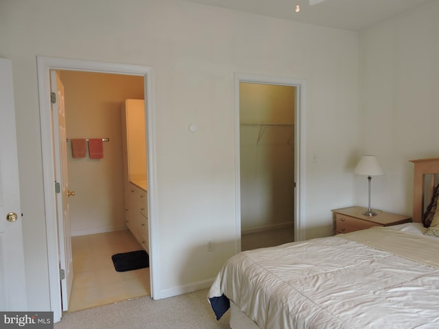 bedroom with ensuite bath, a spacious closet, a closet, and light colored carpet