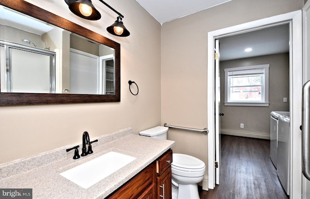 bathroom with toilet, vanity, wood-type flooring, separate washer and dryer, and a shower with door