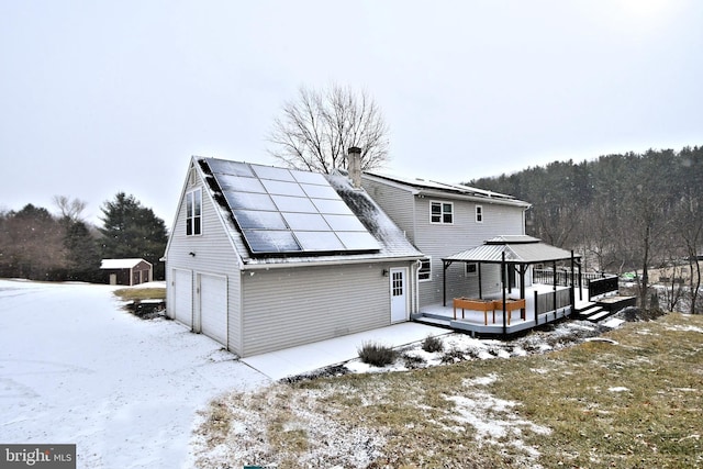 snow covered property featuring a gazebo, solar panels, and a garage