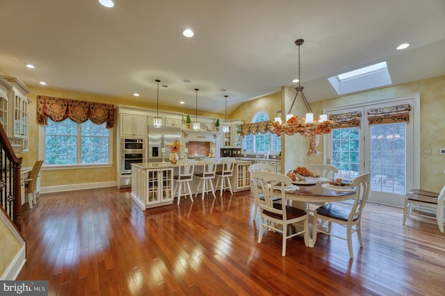 dining area with hardwood / wood-style floors, a notable chandelier, and a skylight