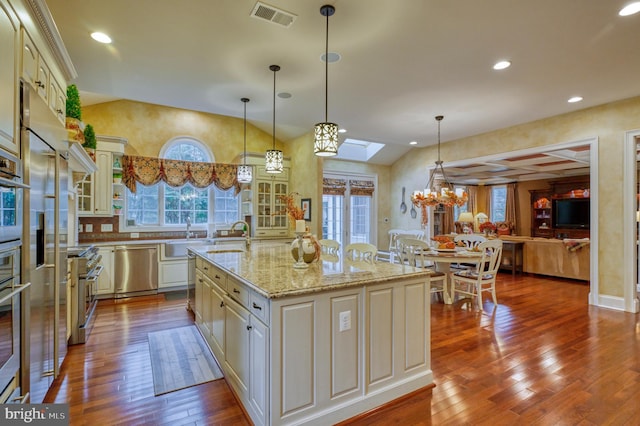 kitchen with appliances with stainless steel finishes, a skylight, an island with sink, wood-type flooring, and hanging light fixtures