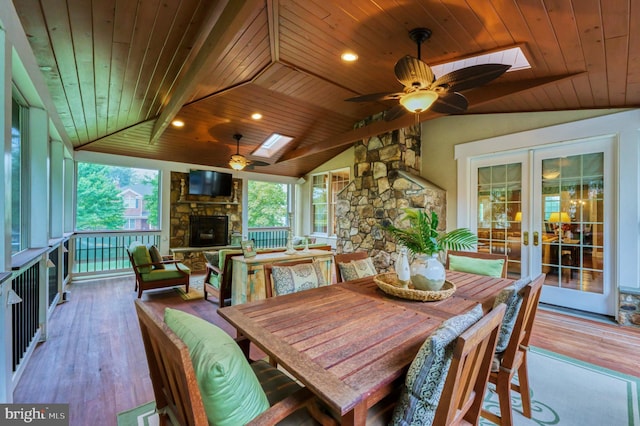 dining space with french doors, a healthy amount of sunlight, a stone fireplace, and vaulted ceiling with skylight