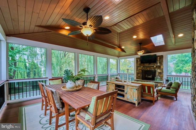 sunroom / solarium with ceiling fan, vaulted ceiling with skylight, a fireplace, wooden ceiling, and beverage cooler