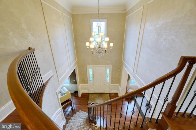 staircase with an inviting chandelier, hardwood / wood-style floors, ornamental molding, and a high ceiling