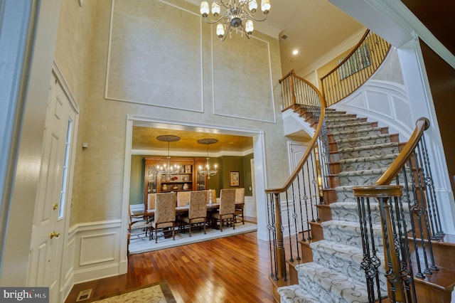 foyer entrance featuring a notable chandelier, crown molding, a towering ceiling, and hardwood / wood-style flooring