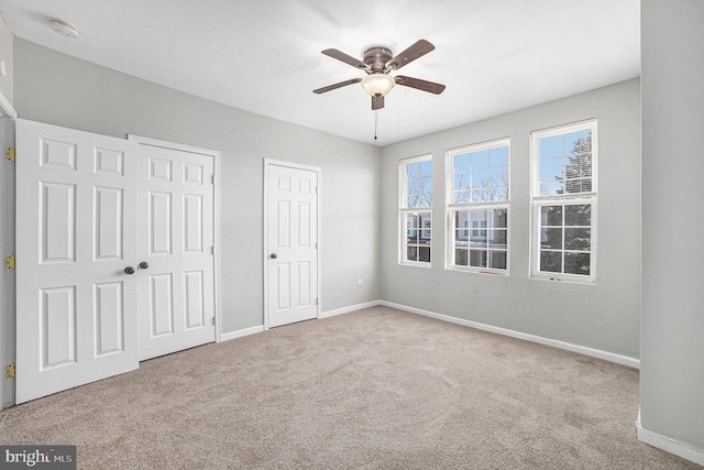 unfurnished bedroom featuring ceiling fan, light carpet, and two closets