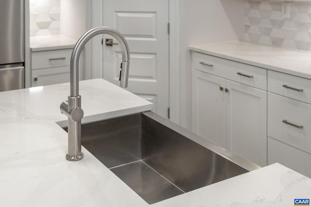 room details with white cabinetry, sink, light stone countertops, stainless steel fridge, and decorative backsplash