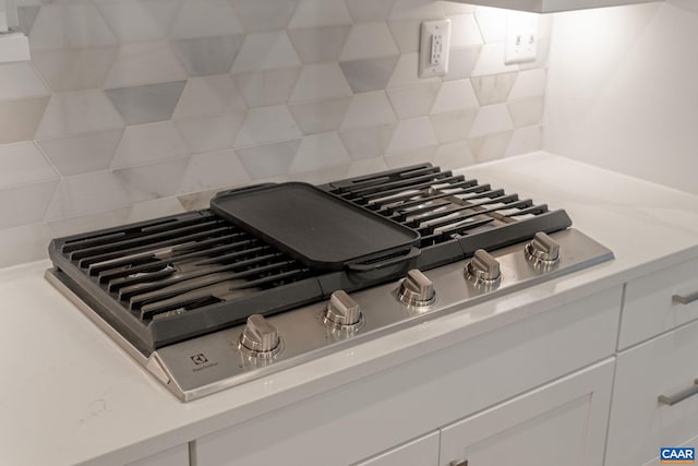 details with decorative backsplash, white cabinetry, and stainless steel gas stovetop