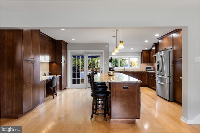 kitchen featuring sink, stainless steel fridge, a center island, light stone counters, and decorative light fixtures