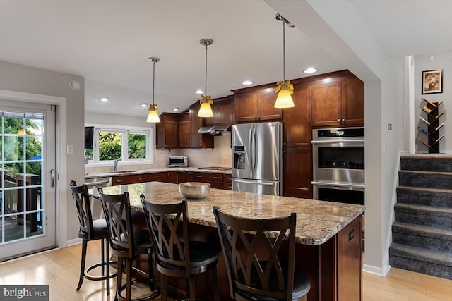 kitchen with stainless steel appliances, light stone countertops, a center island, and sink