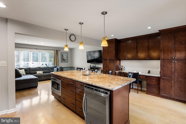 kitchen with a center island, stainless steel microwave, light stone counters, wine cooler, and decorative light fixtures