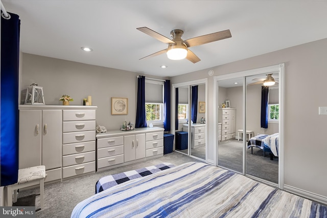 bedroom featuring multiple windows, light carpet, two closets, and ceiling fan