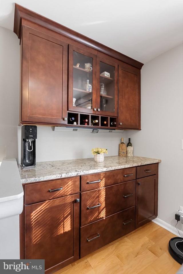 bar with dark brown cabinetry, light stone countertops, and light hardwood / wood-style flooring