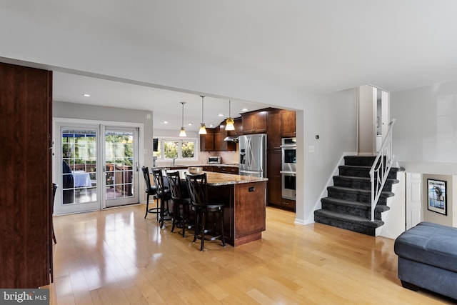 kitchen featuring a breakfast bar, light stone countertops, a kitchen island, stainless steel fridge with ice dispenser, and decorative light fixtures