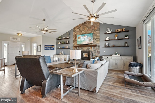 living room with lofted ceiling, a wealth of natural light, light hardwood / wood-style flooring, and a stone fireplace