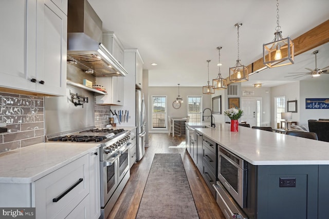 kitchen featuring pendant lighting, wall chimney range hood, a large island, appliances with stainless steel finishes, and white cabinets