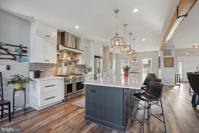 kitchen with wall chimney exhaust hood, white cabinetry, appliances with stainless steel finishes, a kitchen breakfast bar, and a large island