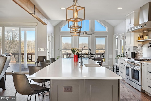 kitchen with decorative light fixtures, vaulted ceiling, an island with sink, and range with two ovens