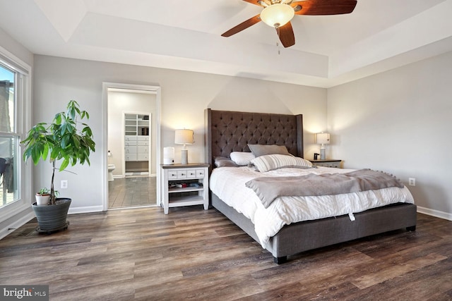 bedroom with ensuite bathroom, dark wood-type flooring, ceiling fan, and a tray ceiling