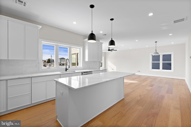 kitchen with visible vents, a sink, a kitchen island, backsplash, and light wood finished floors