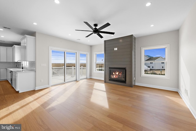 unfurnished living room with baseboards, a fireplace, recessed lighting, a sink, and light wood-style floors