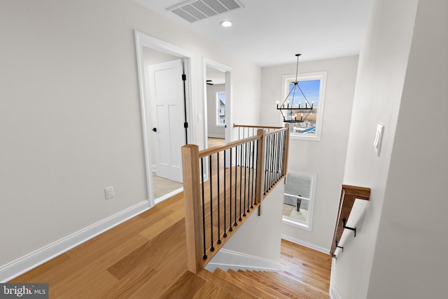 hall with an upstairs landing, visible vents, light wood finished floors, and baseboards