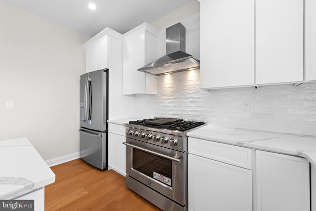 kitchen featuring light wood finished floors, tasteful backsplash, wall chimney range hood, appliances with stainless steel finishes, and white cabinetry