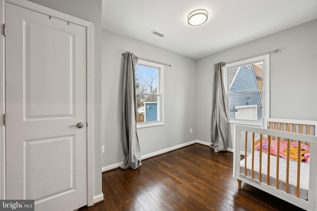 bedroom with dark wood-type flooring, multiple windows, and a crib