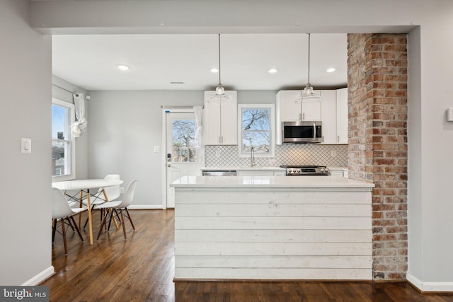 kitchen featuring tasteful backsplash, white cabinetry, hanging light fixtures, dark wood-type flooring, and stainless steel appliances