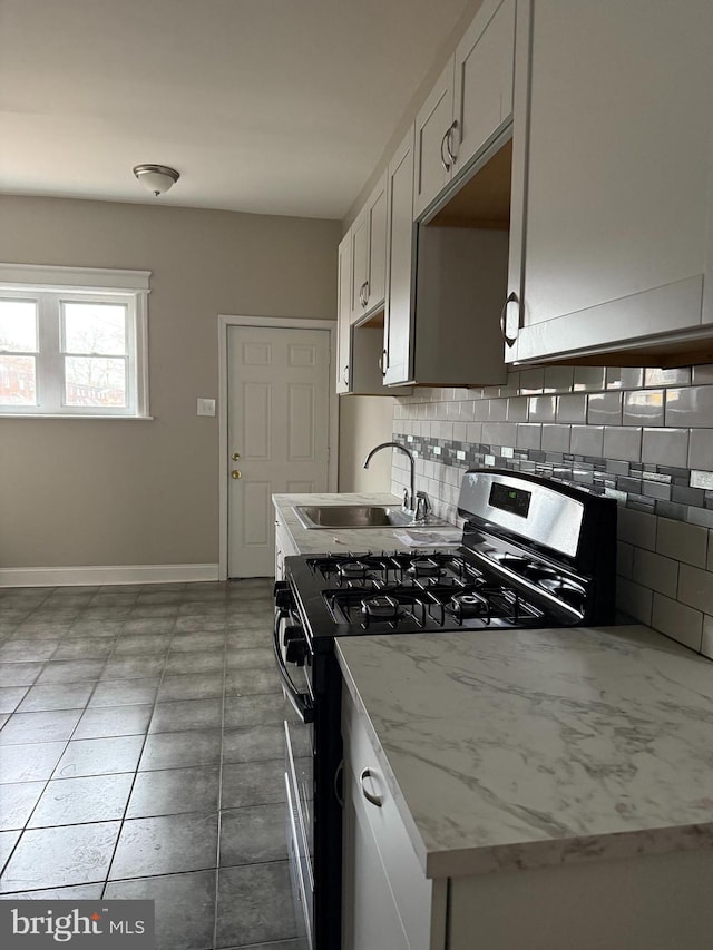 kitchen with backsplash, black range with gas stovetop, sink, light stone countertops, and white cabinetry