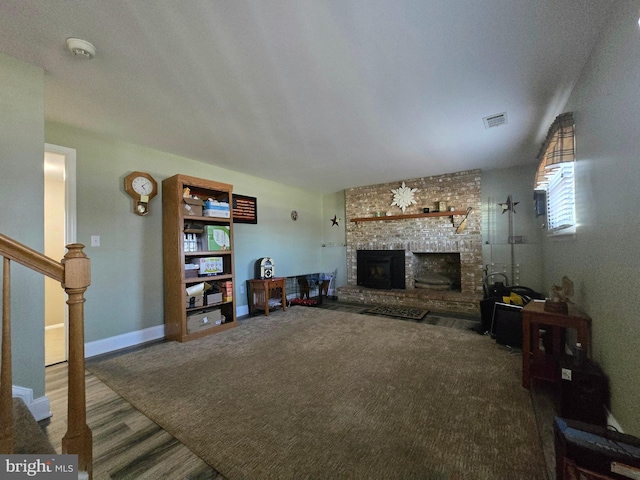 carpeted living area with a brick fireplace, baseboards, stairs, and visible vents